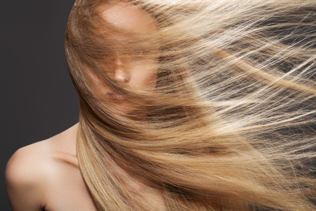 Bien-être et spa. Modèle de femme sensuelle avec des cheveux blond foncé volants balayés par le vent sur fond gris.