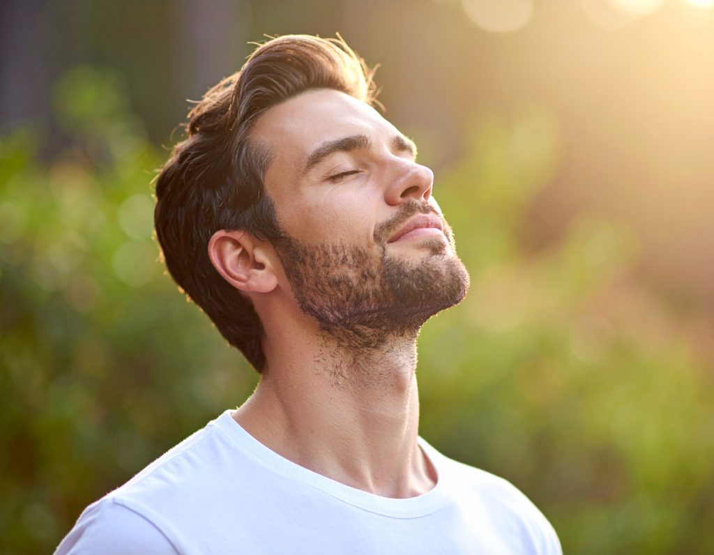 Hombre en la naturaleza respirando profundamente con los pulmones expandidos y los ojos cerrados.
