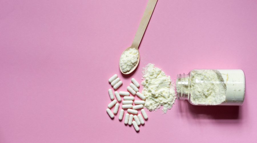 Collageenpoeder in een lepel en in een potje, en pillen op een roze ondergrond. Roze achtergrond met ruimte.