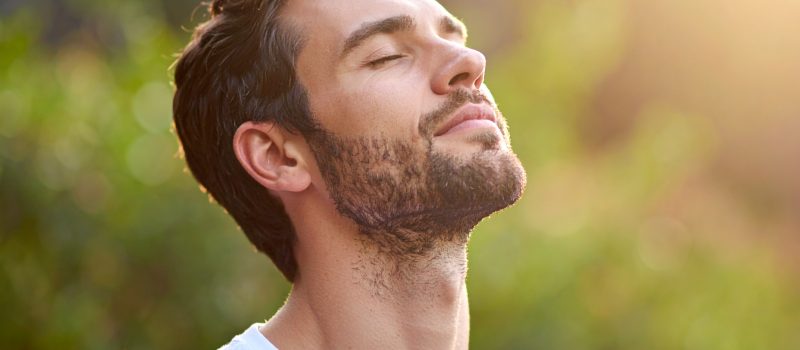 自然の中で目を閉じて肺を膨らませて深く呼吸する男性
