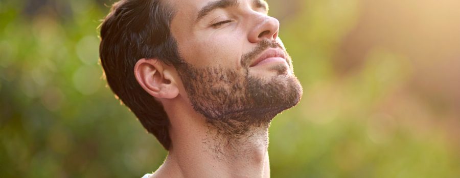 Mann in der Natur atmet tief mit erweiterten Lungen und geschlossenen Augen